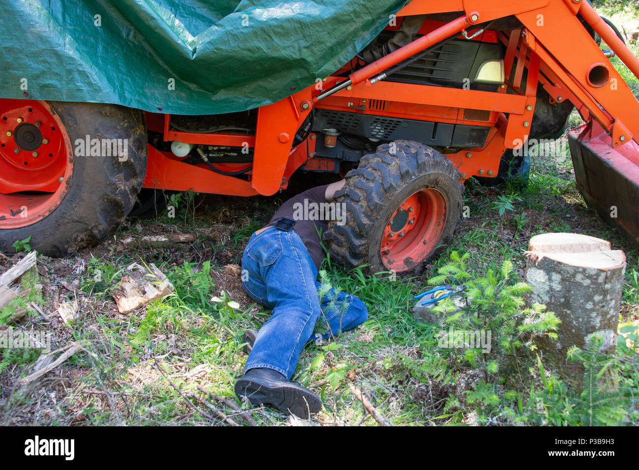Un meccanico sul terreno al di sotto di un trattore di effettuare riparazioni in sede di lavoro nelle Montagne Adirondack, NY USA Foto Stock