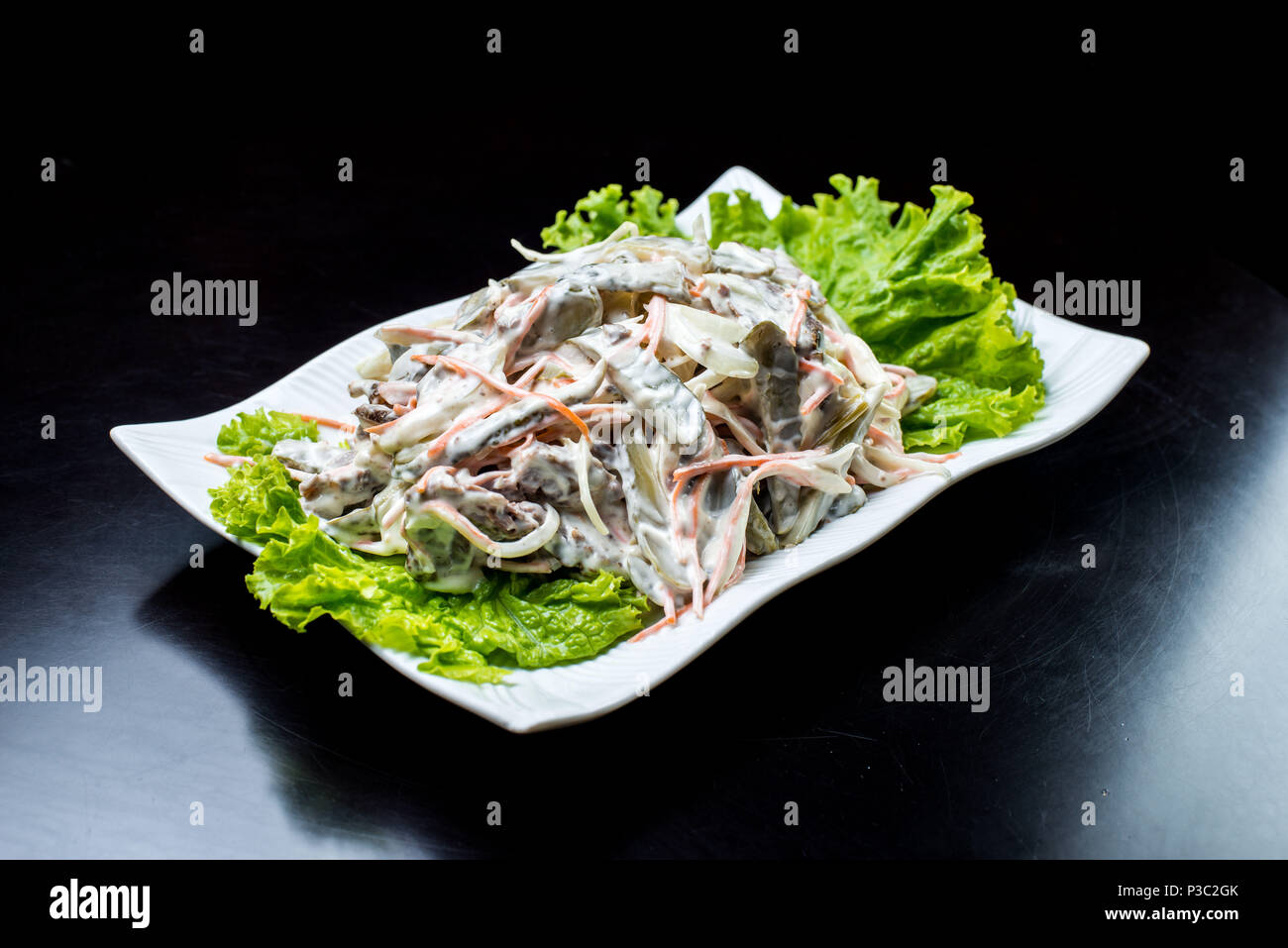 La cucina cinese, con insalata di funghi, carni bovine fritto, sottaceti, lattuga in una piastra bianca su sfondo nero Foto Stock