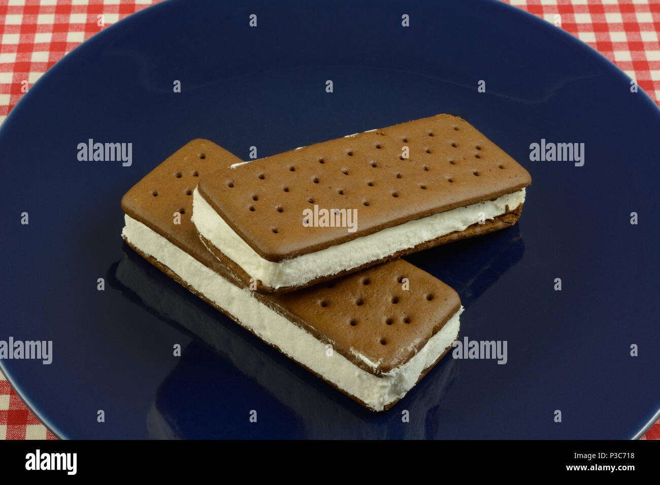 Due congelati ice cream sandwich sulla piastra blu su bianco e rosso tovaglia a scacchi Foto Stock