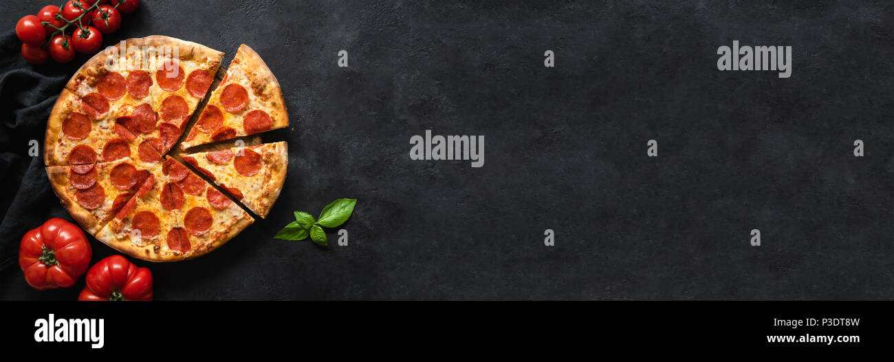 Gustosa salsiccia per pizza pizza e cottura Ingredienti Pomodori basilico nero su sfondo di calcestruzzo. Vista superiore della salsiccia per pizza calda pizza. Banner Foto Stock