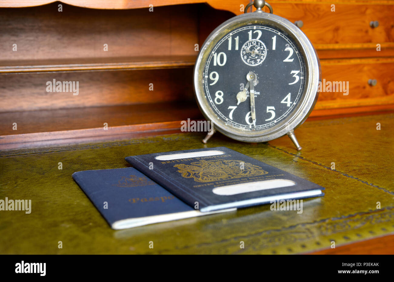 Blu di passaporto britannico e australian passportwith vecchio orologio sveglia su legni antichi scrivania Foto Stock