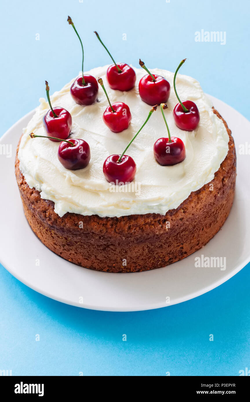 In casa la panna acida torta con la glassa di formaggio cremoso decorate con fresche ciliege mature su sfondo azzurro. Foto Stock