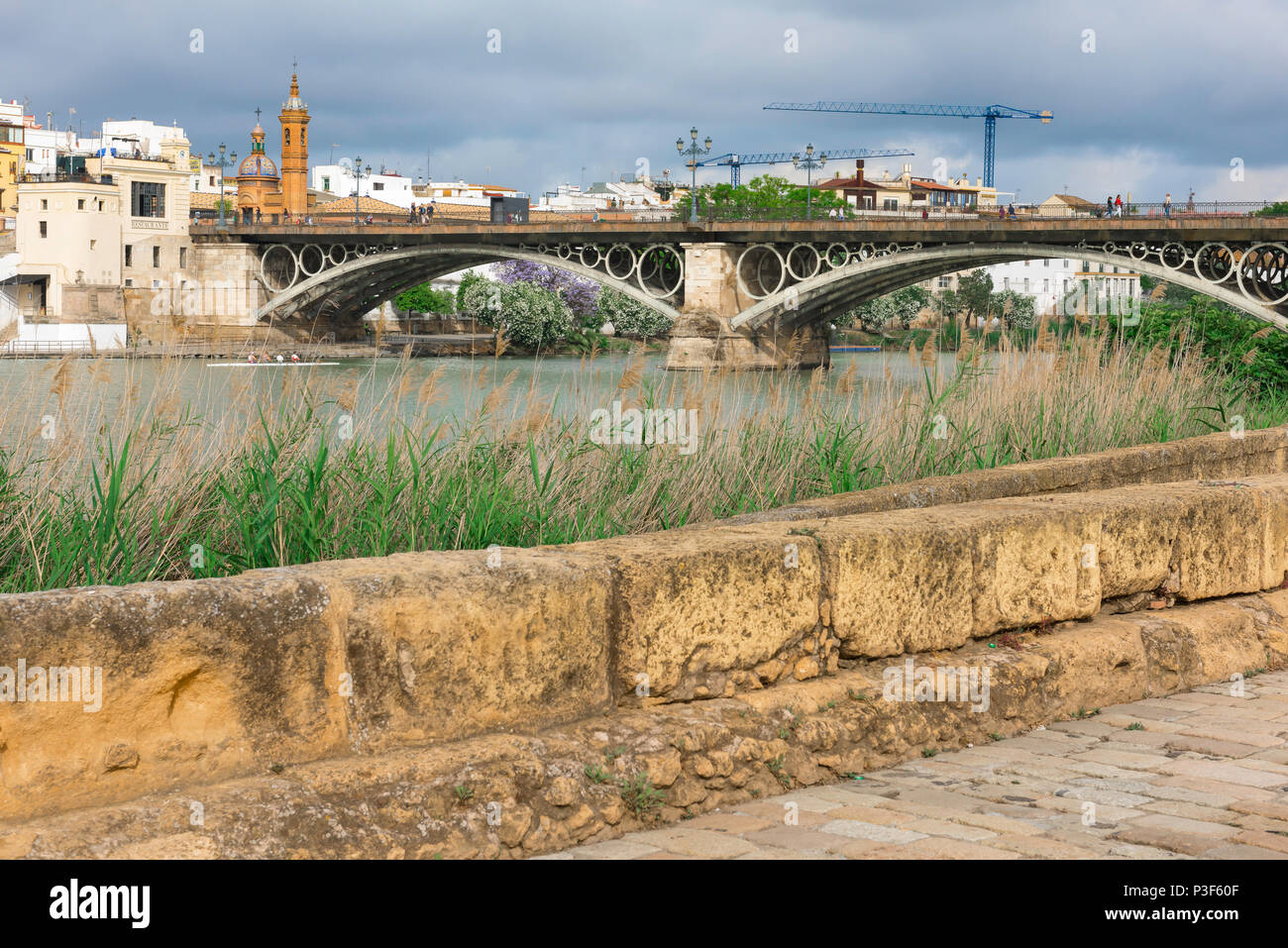 Il fiume di Siviglia, vista attraverso il Rio Guadalquivir verso il Barrio Triana di Siviglia con una sezione della cinta muraria medievale in primo piano, Spagna. Foto Stock