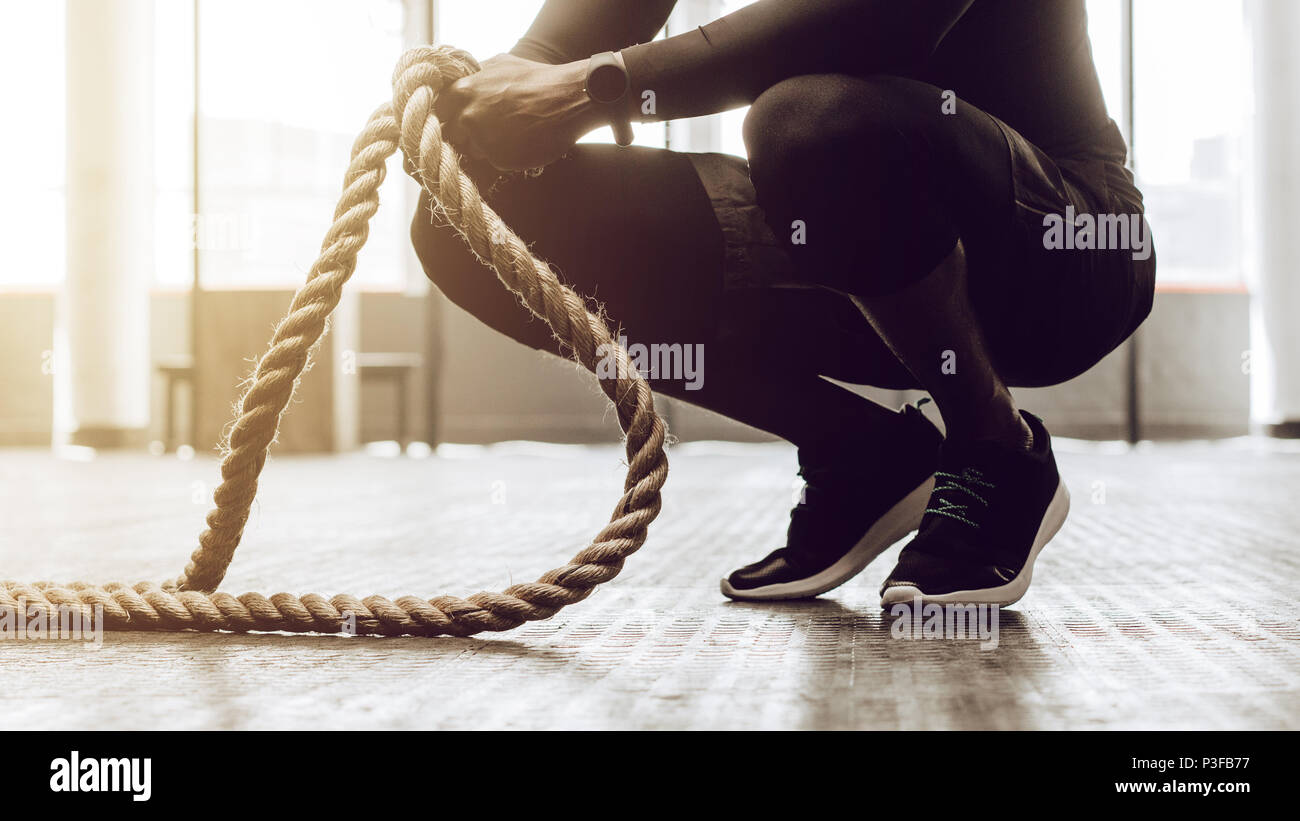 Close up di un uomo seduto sulle sue dita di presa di un paio di battaglia di corde di allenamento. Crossfit guy in palestra lavora con fune di fitness. Foto Stock