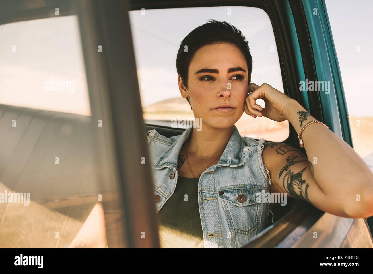 La donna su un viaggio in auto. Donna con tatuaggi su bracci guardando fuori della sua automobile seduto alla finestra. Foto Stock
