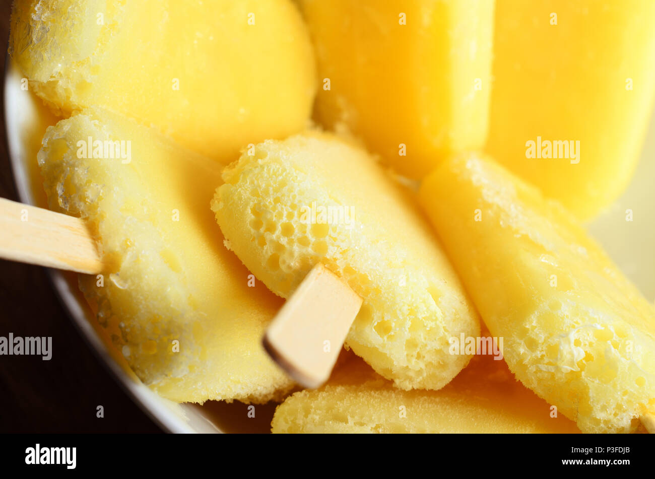 Tettuccio di close up di giallo ananas ghiaccioli con bastoni di legno, capovolta e raggruppati in una ciotola bianco. Foto Stock