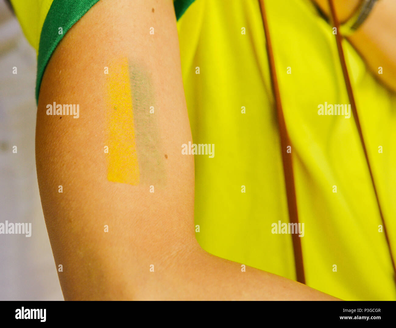 Tatuaggio un braccio con il giallo e il verde che simboleggia il calcio brasiliano o soccer team, con la mitica Maglia gialla, sostenitore della coppa del mondo di concetto Foto Stock