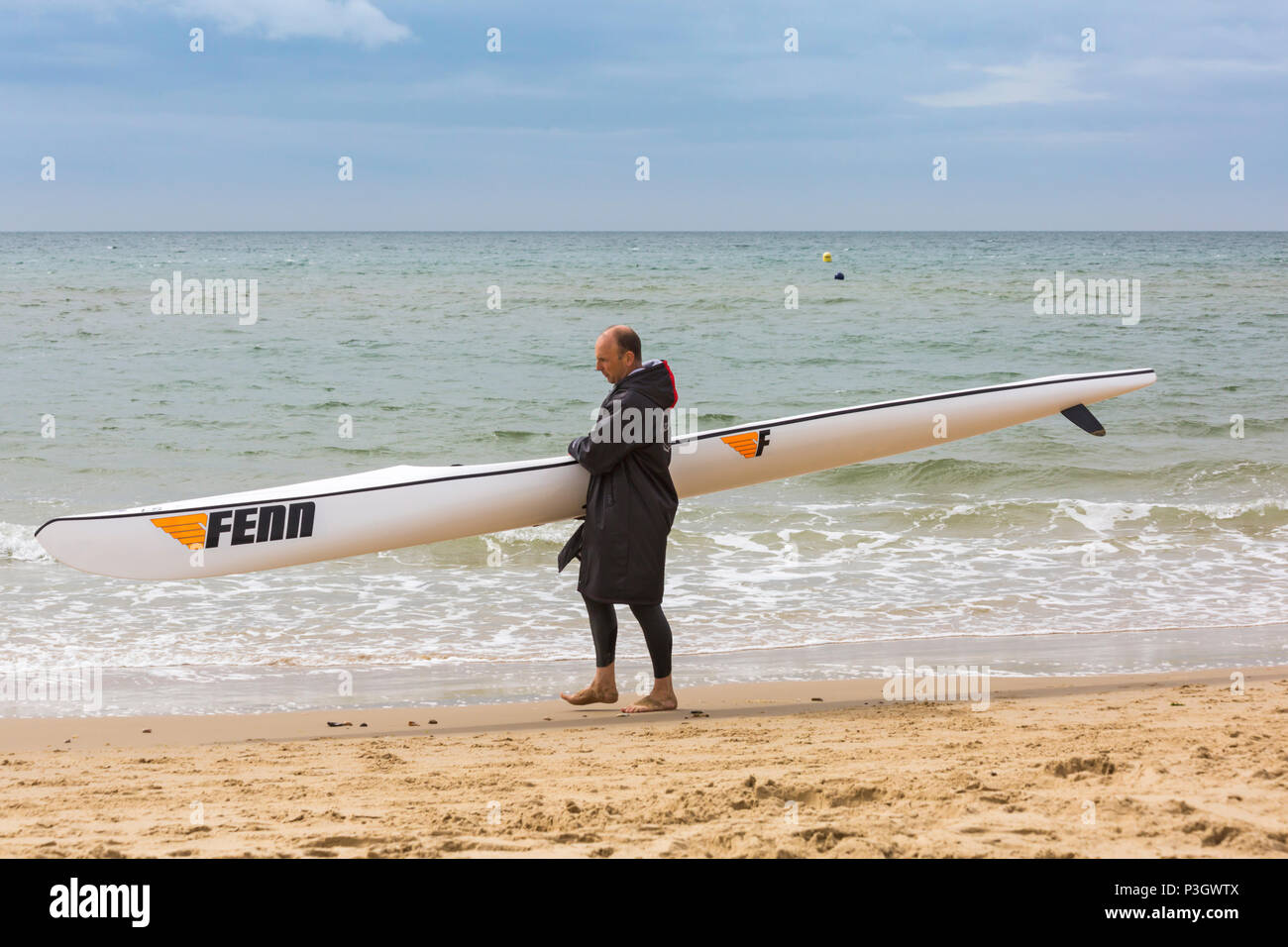 Uomo che porta un surf ski surfski lungo il litorale di Branksome Chine, Poole, Dorset, England Regno Unito nel mese di giugno Foto Stock