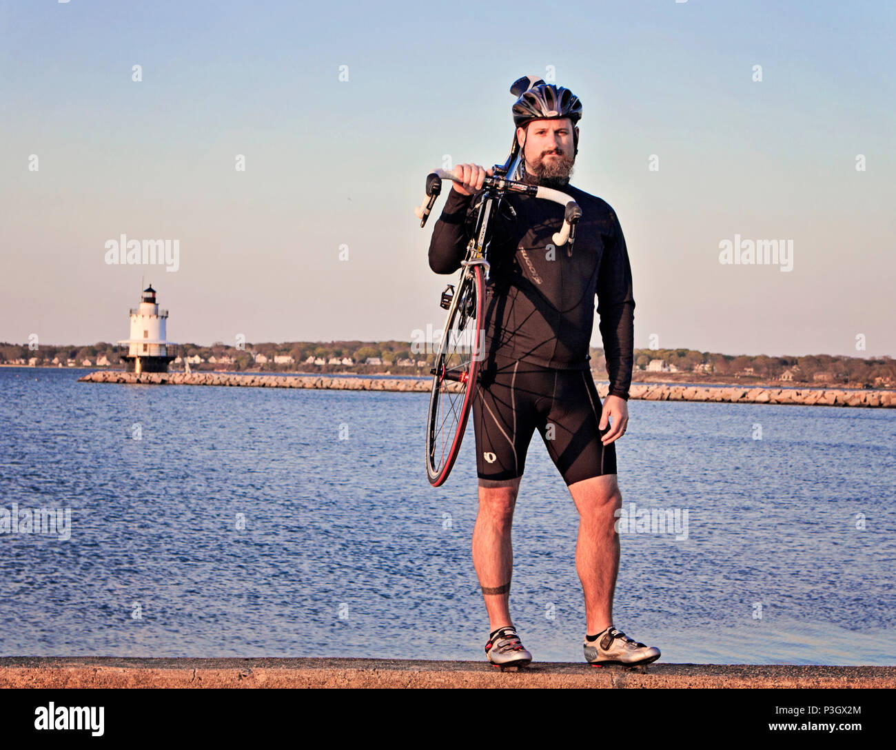 Un maschio ciclista sta per un ritratto con un faro in background, Portland, Maine. Foto Stock