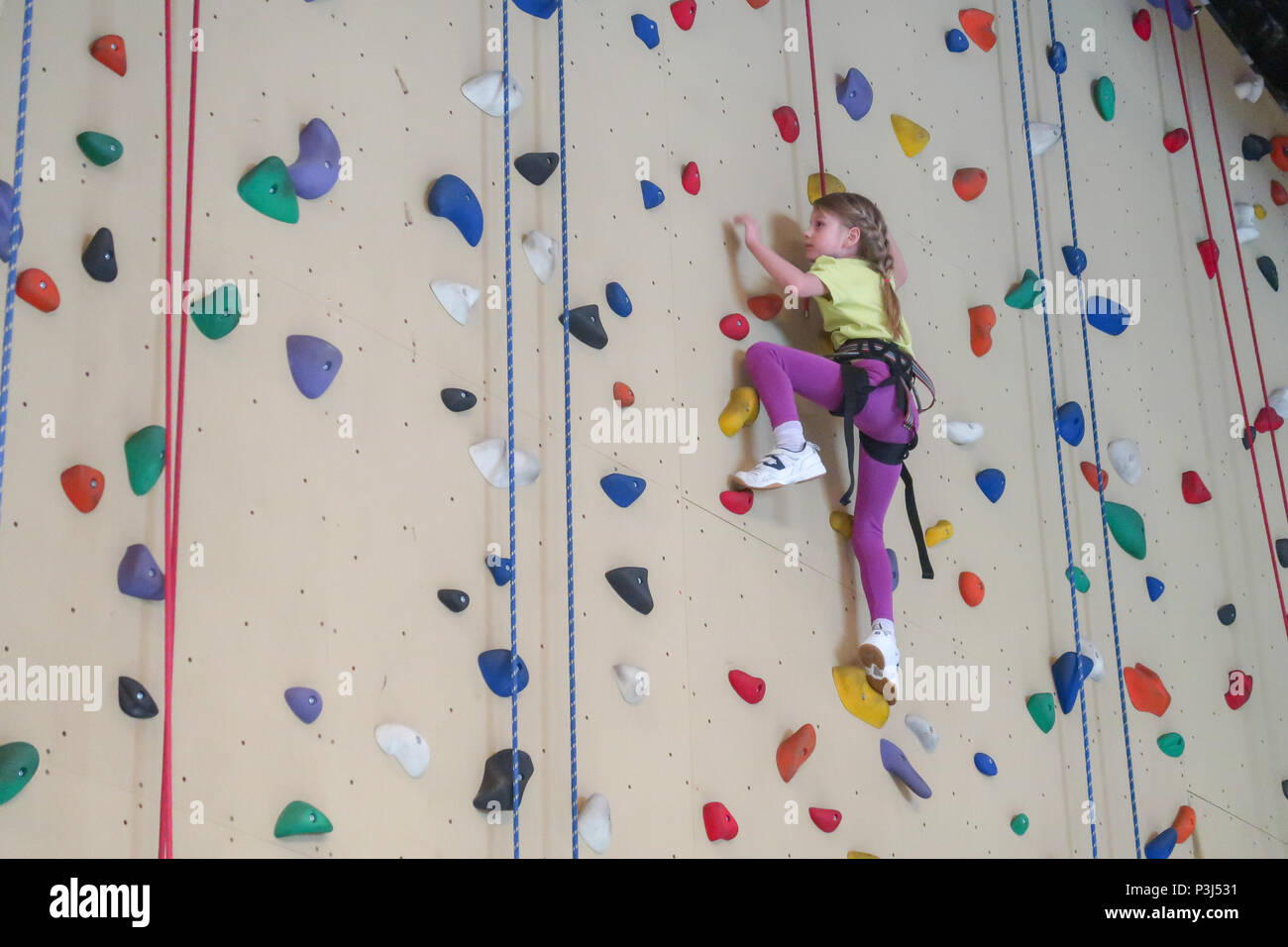 Un 7 anno vecchia ragazza si arrampica su una parete di arrampicata Foto Stock