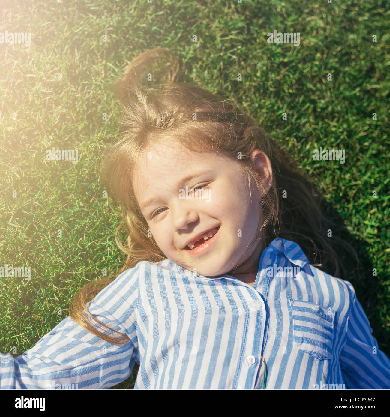 Bambina guardando la telecamera, sorridente e giacente sull'erba. In estate il tempo libero. Ragazza senza denti frontali. Foto Stock