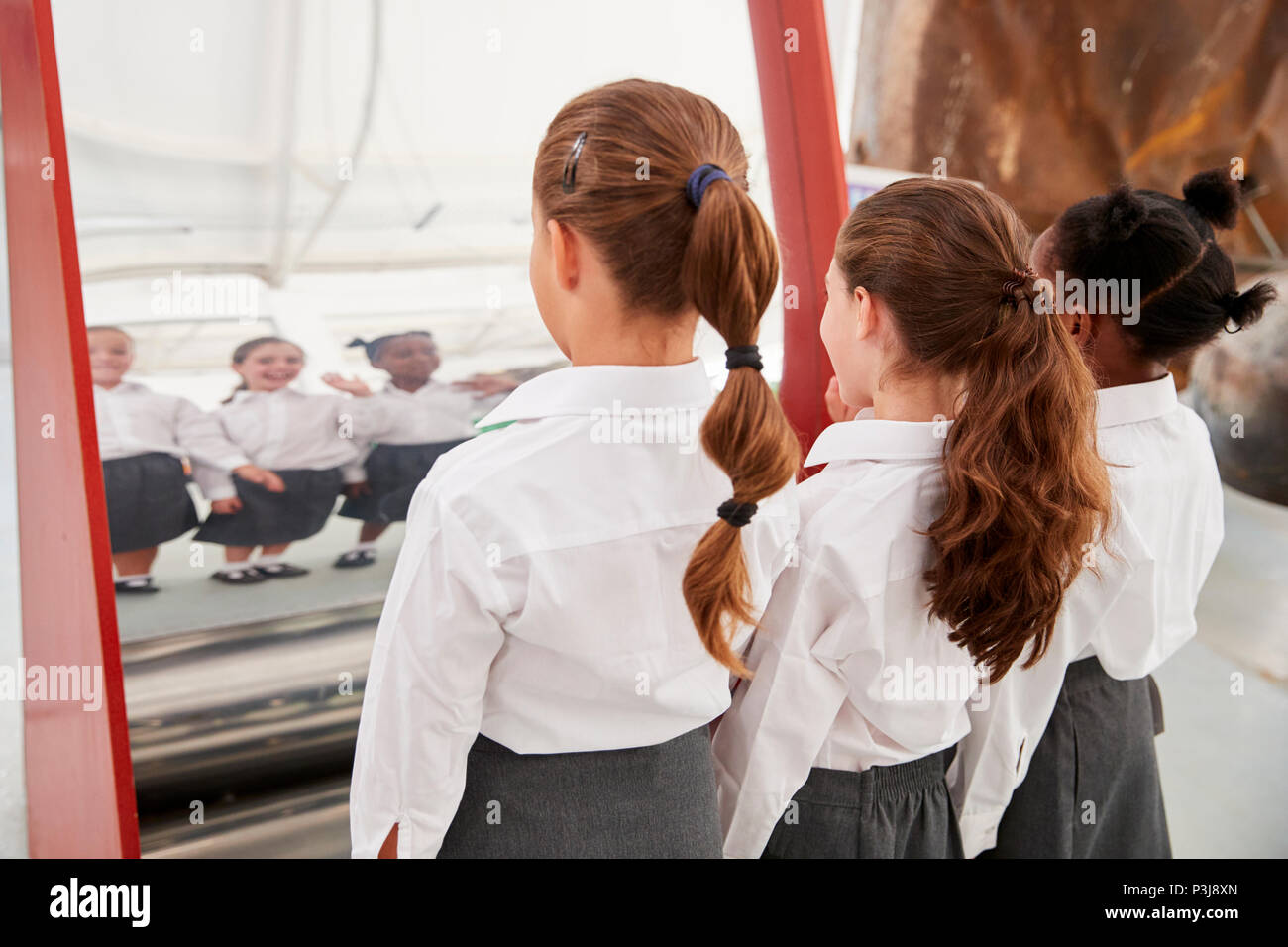 Studentesse guardando in uno specchio curvo in un centro scientifico Foto Stock