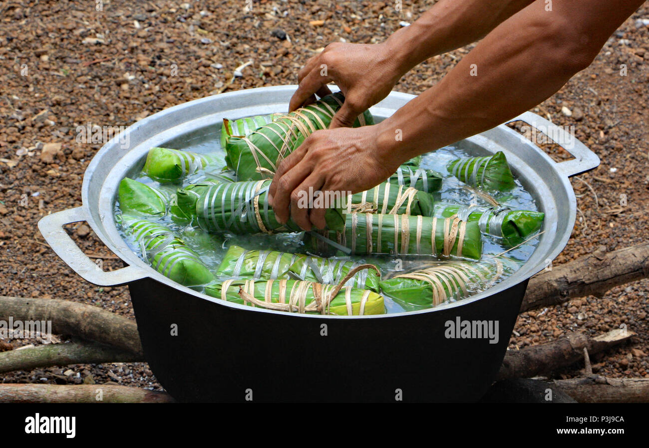 Il giorno prima di un cambogiano di matrimonio la famiglia prepara il banchetto di nozze. Questo uomo è la cottura del riso e dolci avvolti in foglie di banana. Foto Stock