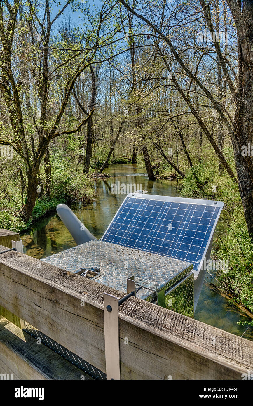 Colpo verticale di un del pannello solare che alimenta un Smoky Mountain stazione di ricerca impostare la prossima ad una corrente che passa attraverso gli alberi. Foto Stock