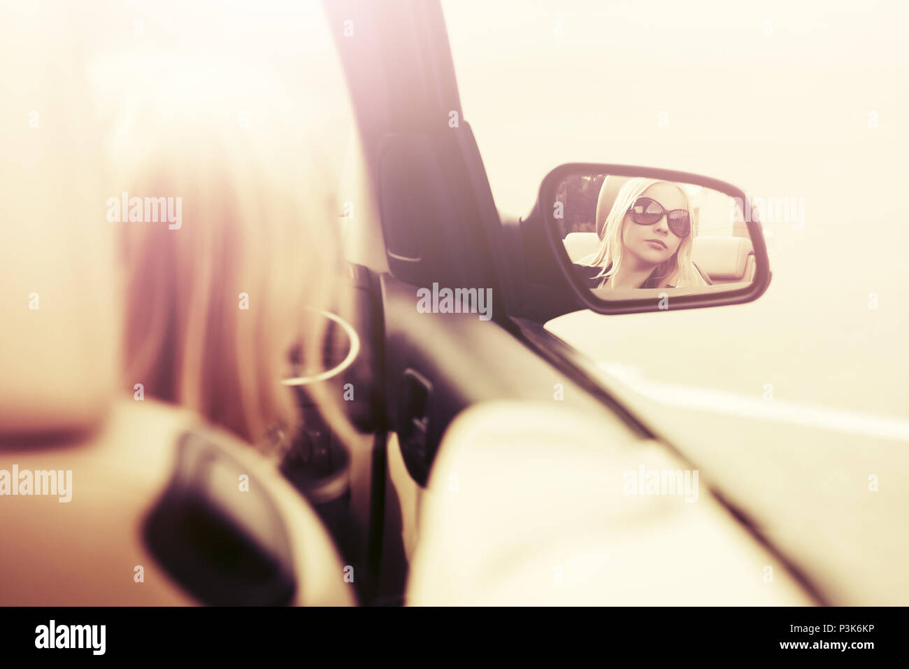 Donna bionda in occhiali da sole cercando in auto lo specchietto retrovisore Foto Stock