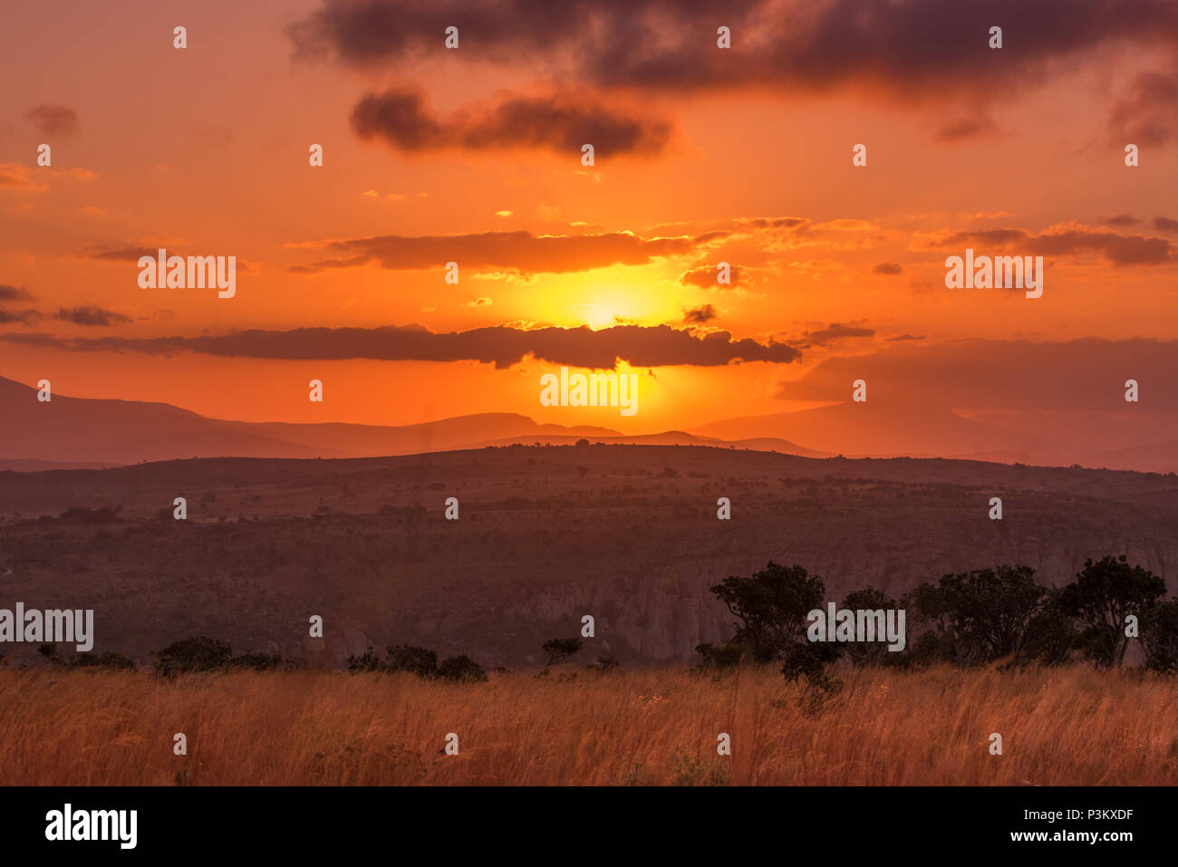 Il sole brilla dietro le nuvole in un intenso tramonto al di sopra di un Africano paesaggio di colline, cliffside e savannah a Blyde River Canyon a Mpumalanga, Sout Foto Stock