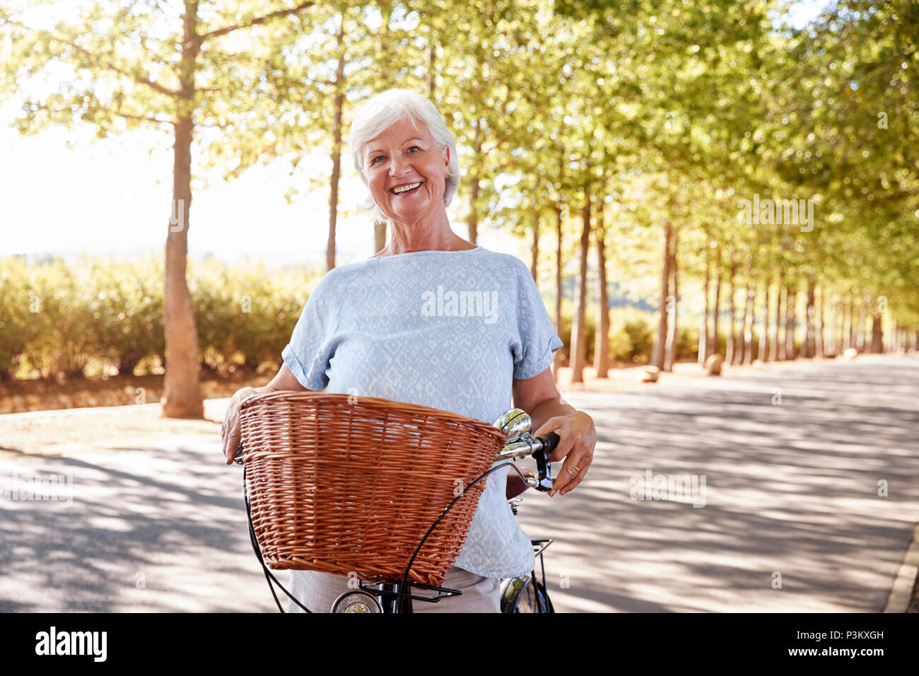 Ritratto di sorridente donna Senior di ciclismo su strada di campagna Foto Stock