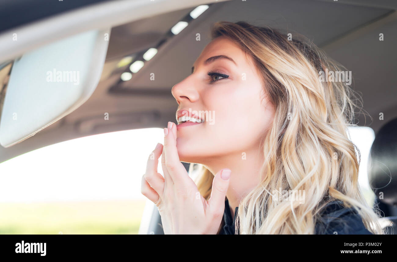 Donna attraente in auto guardando nello specchio della vettura. Foto Stock