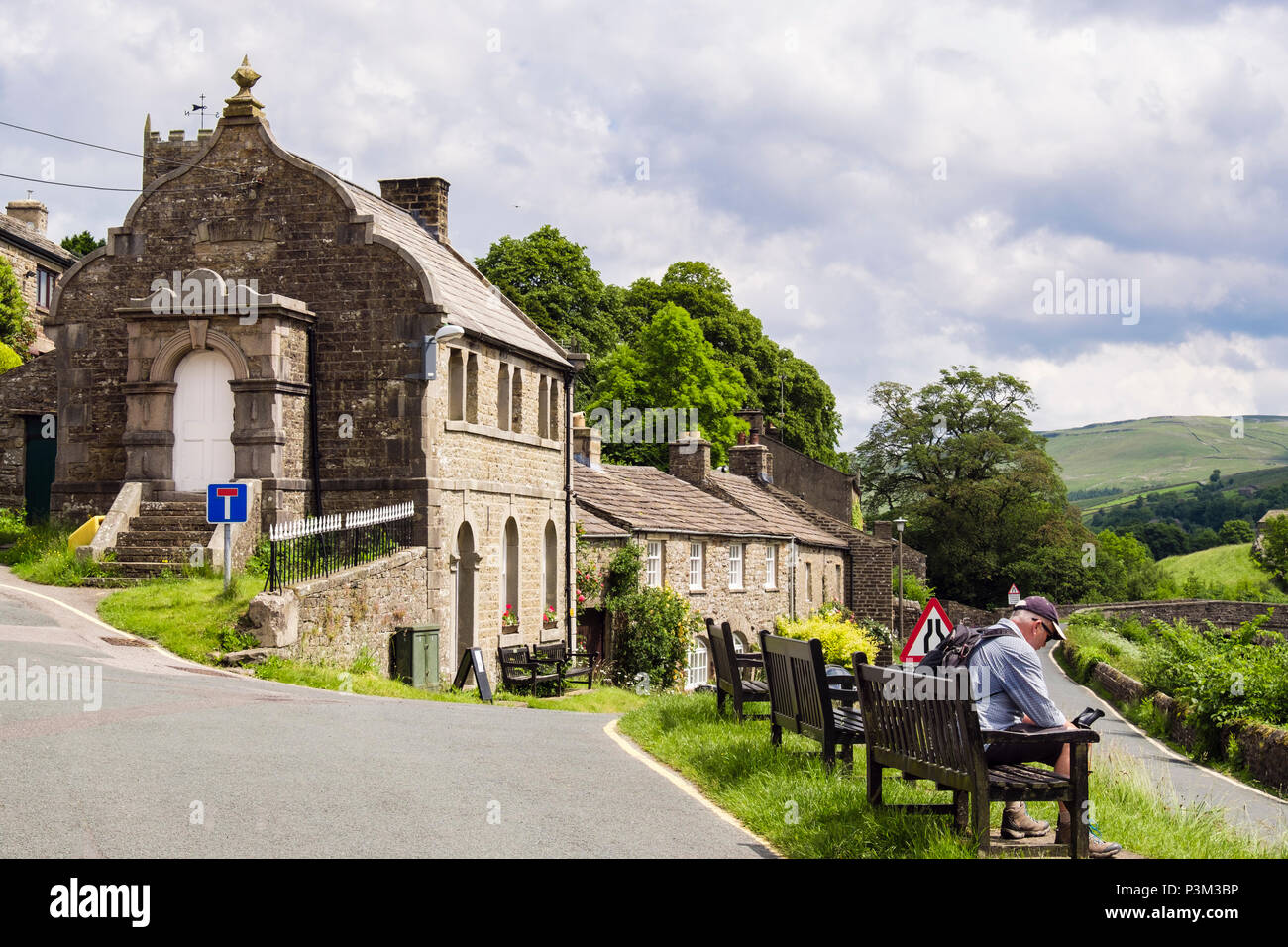 Walker in appoggio su un banco da Muker Istituto letterario in Yorkshire Dales National Park Village di Muker Swaledale North Yorkshire England Regno Unito Gran Bretagna Foto Stock