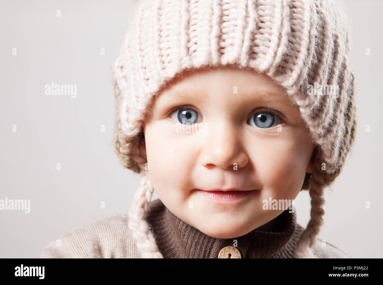 Ritratto di un simpatico baby girl in un enorme marrone berretto lavorato a maglia. Isolato su sfondo bianco. Foto Stock