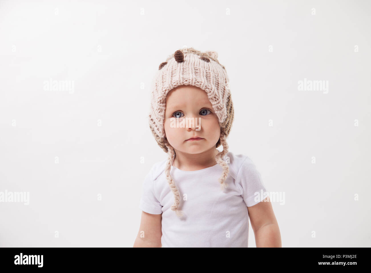 Ritratto di un simpatico baby girl in un enorme marrone berretto lavorato a maglia. Isolato su sfondo bianco. Foto Stock