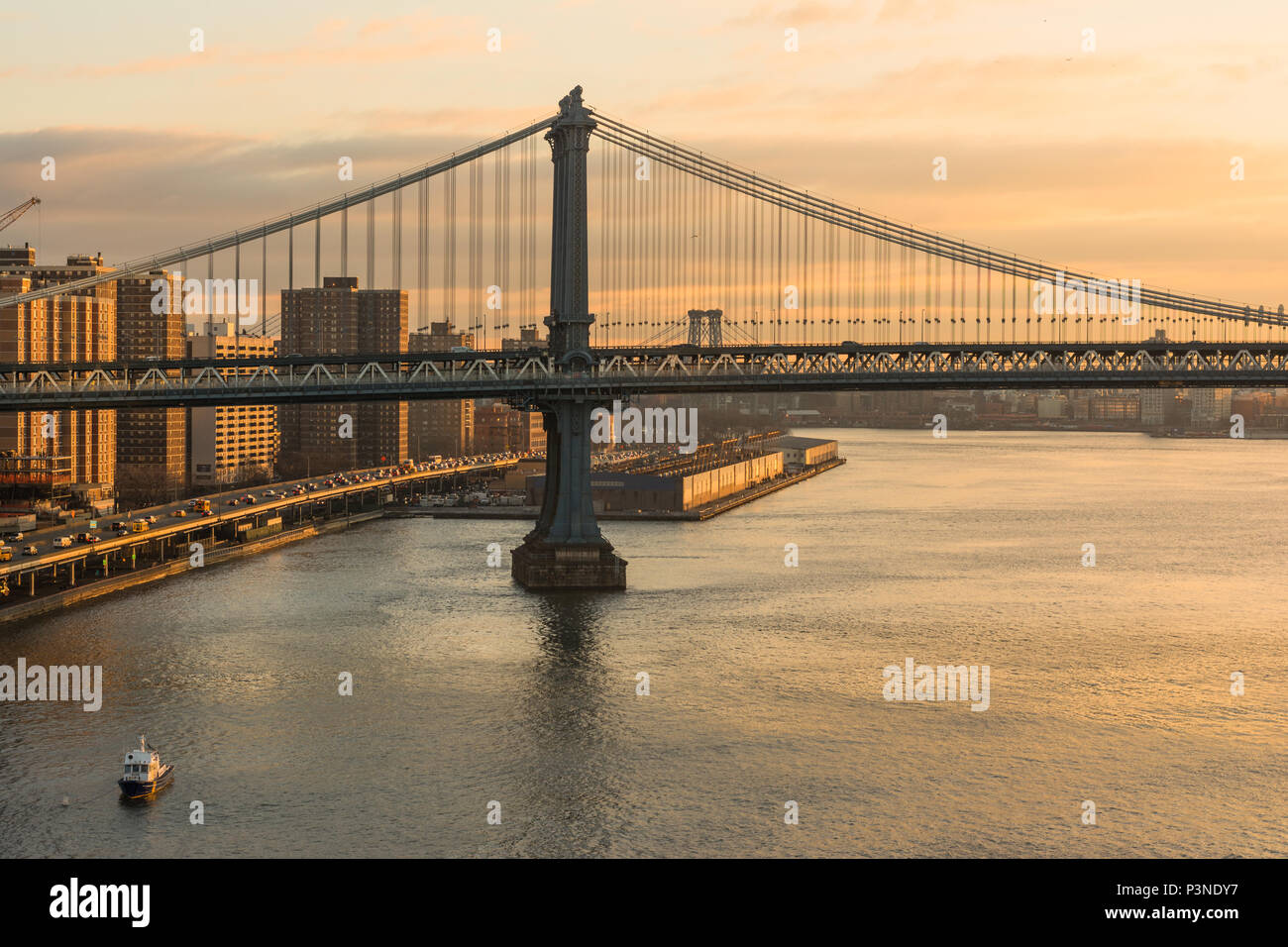 Il sorgere del sole splende il suo colore arancione sul Manhattan Bridge e l'East River. Foto Stock
