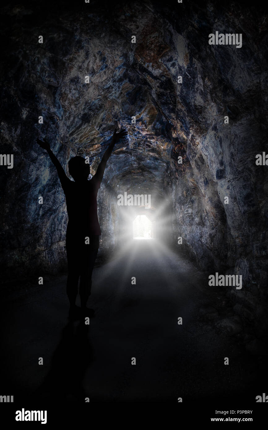 Silhouette di donna alzando le mani con accecante luce alla fine del tunnel. Concetto di conquista di avversità o di successo attraverso gli ostacoli. Foto Stock