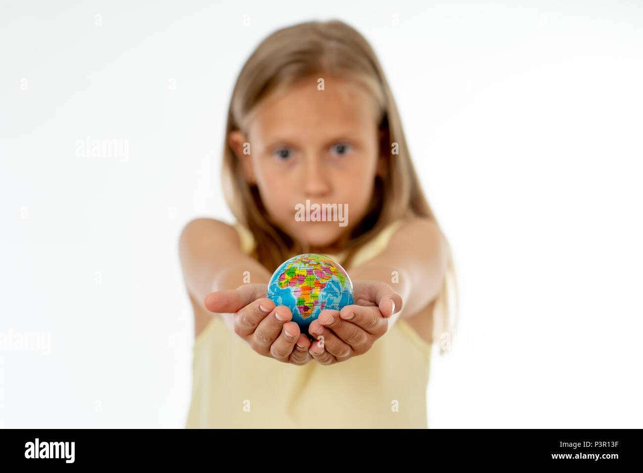 Incantevole carino bambina fuori fuoco tenendo un globo, guardando la fotocamera e sorridente, in piedi su sfondo bianco nel mondo il concetto di apprendimento. Foto Stock