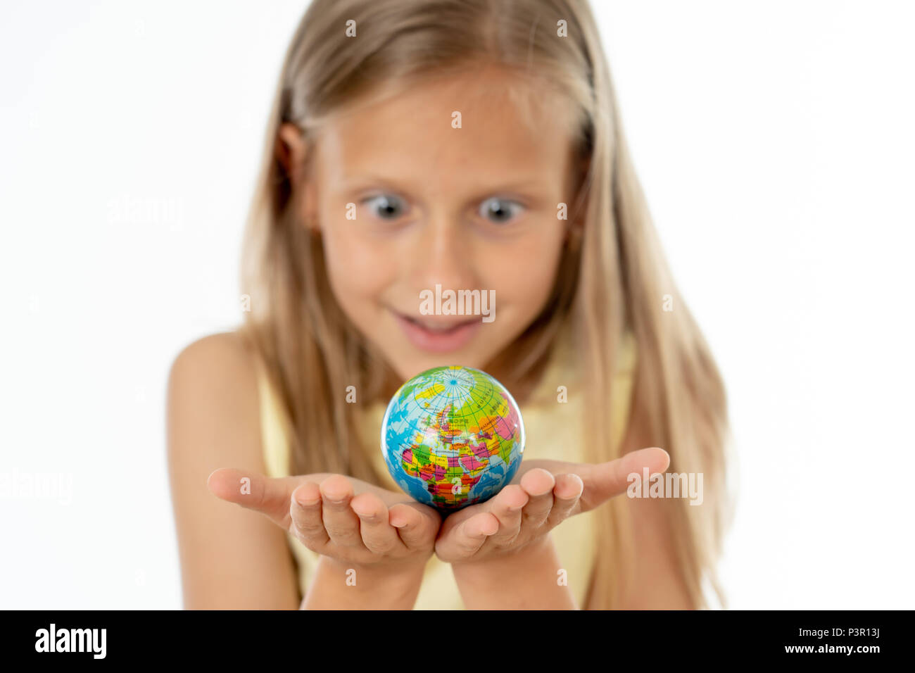 Incantevole carino bambina fuori fuoco tenendo un globo, guardando la fotocamera e sorridente, in piedi su sfondo bianco nel mondo il concetto di apprendimento. Foto Stock