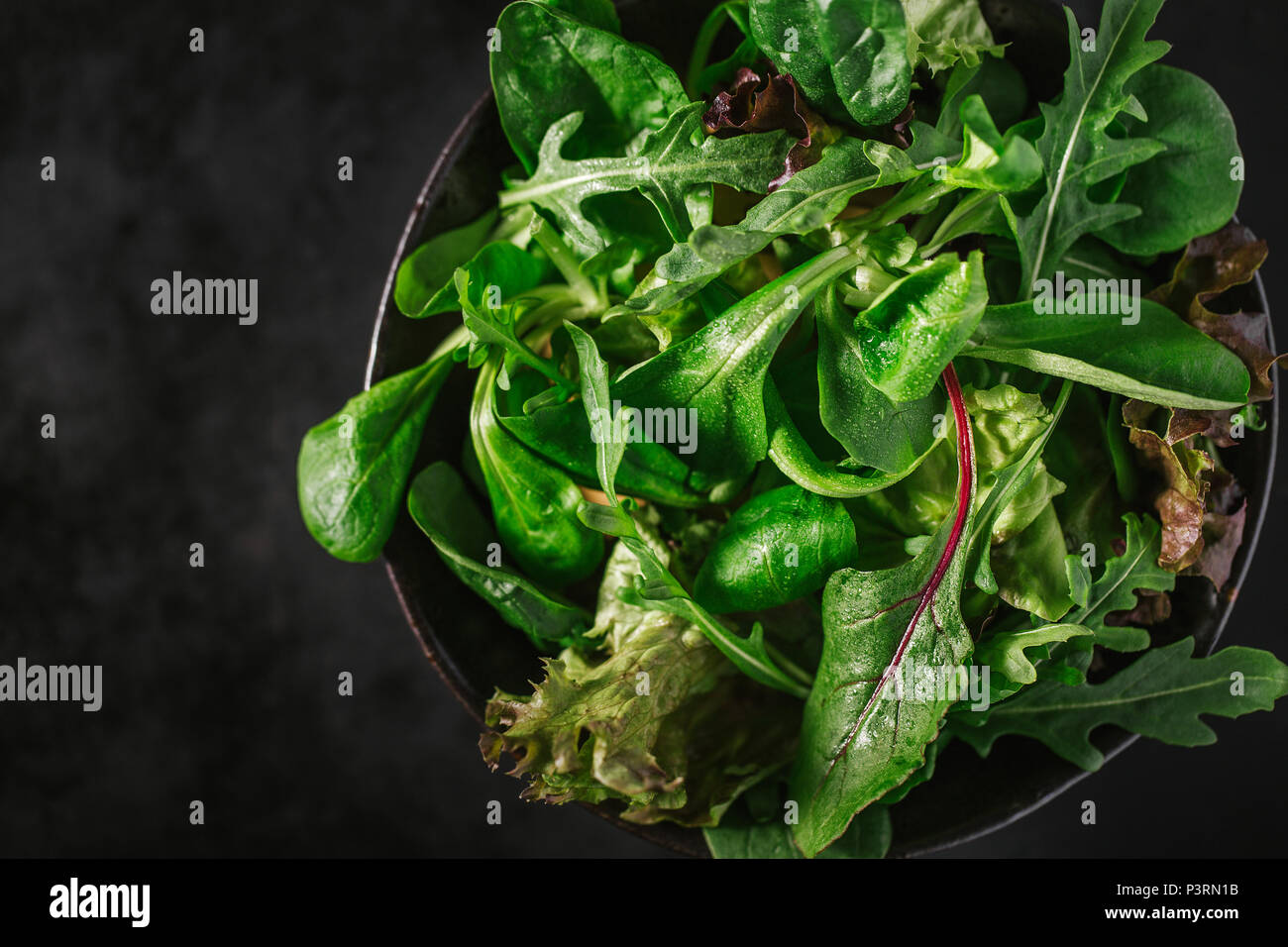 Pronto servito mescolato insalata verde nella ciotola sul tavolo scuro dello sfondo. Vista da sopra. Detox cibo sano concetto Foto Stock