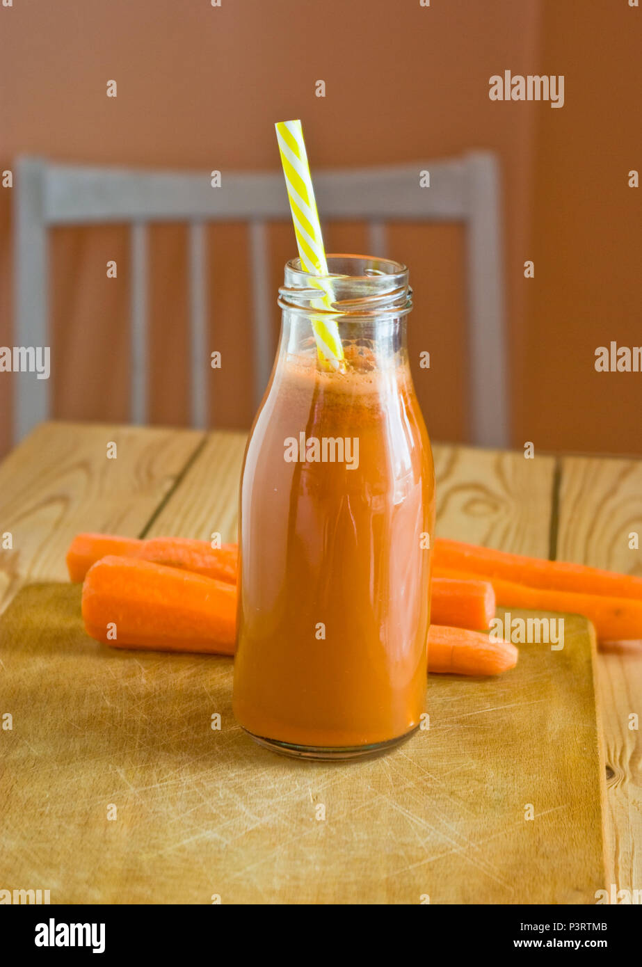 Fresco di succo di carota su un tagliere di legno superficie con carote in cucina Foto Stock