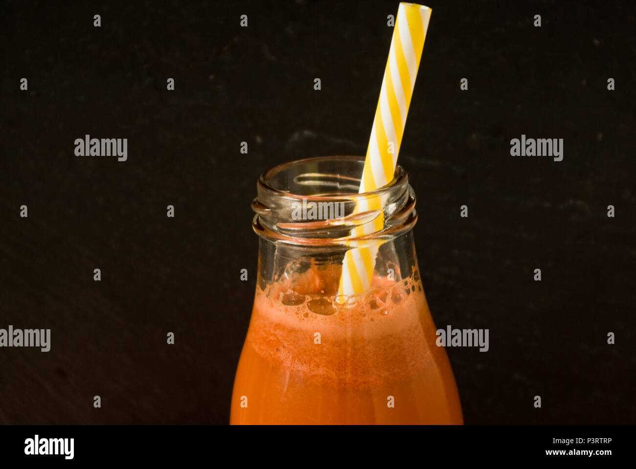 Parte superiore della bottiglia di succo di carota contro uno sfondo nero Foto Stock