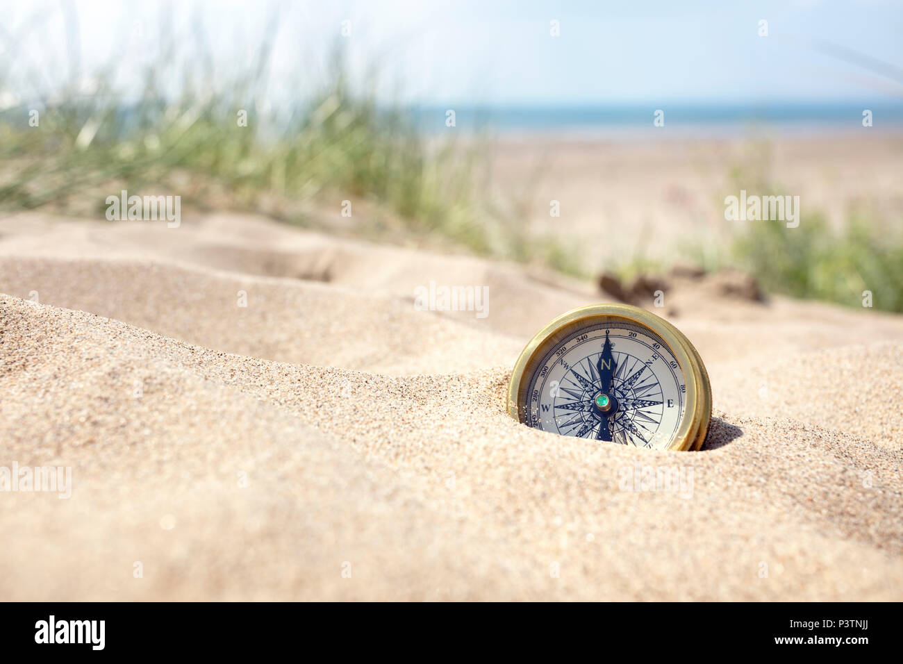 Golden Compass sepolto nella sabbia sulla spiaggia concetto per la perdita o la direzione Foto Stock