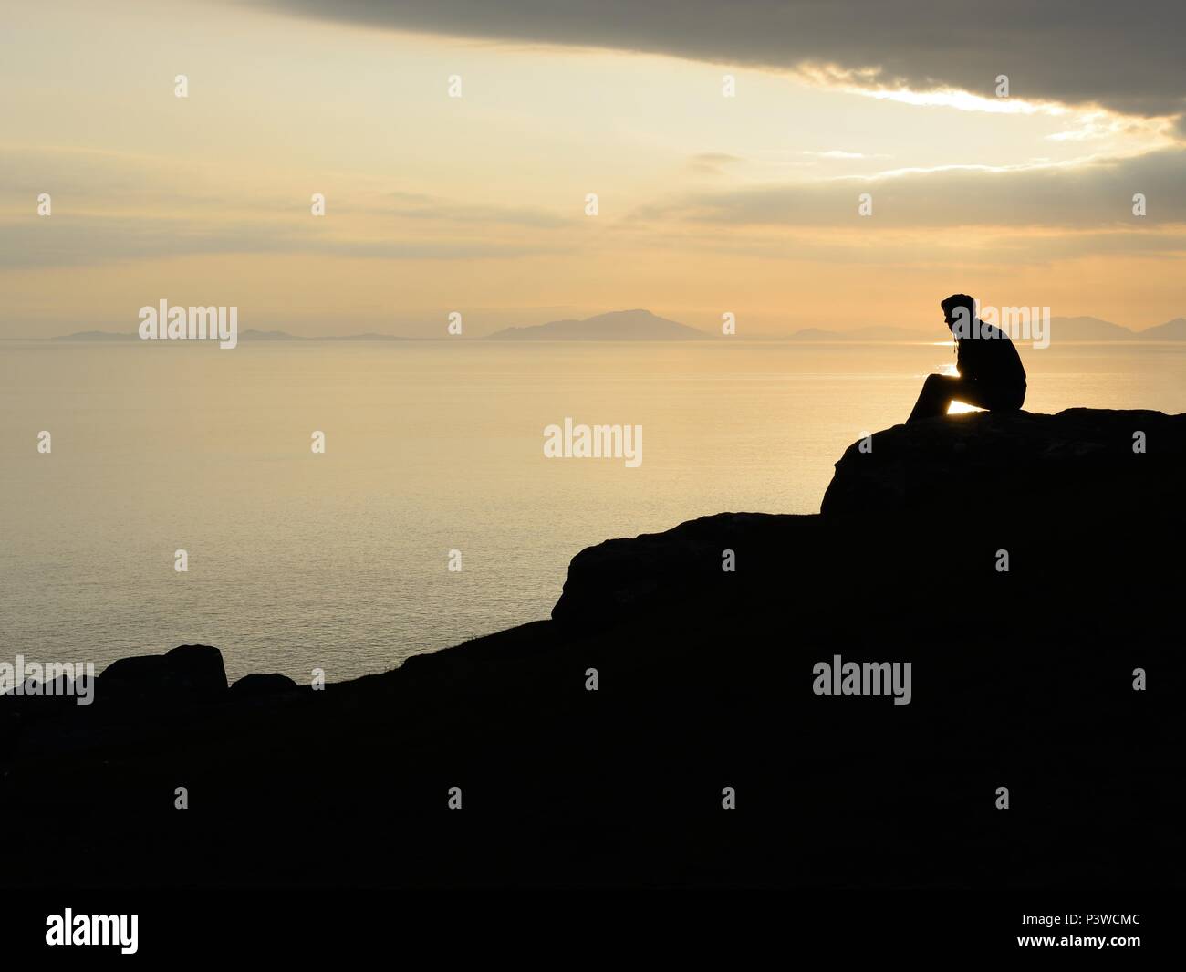 A profilarsi l'uomo guarda al mare al tramonto da una scogliera a Neist punto sull'Isola di Skye in Scozia, Regno Unito Foto Stock