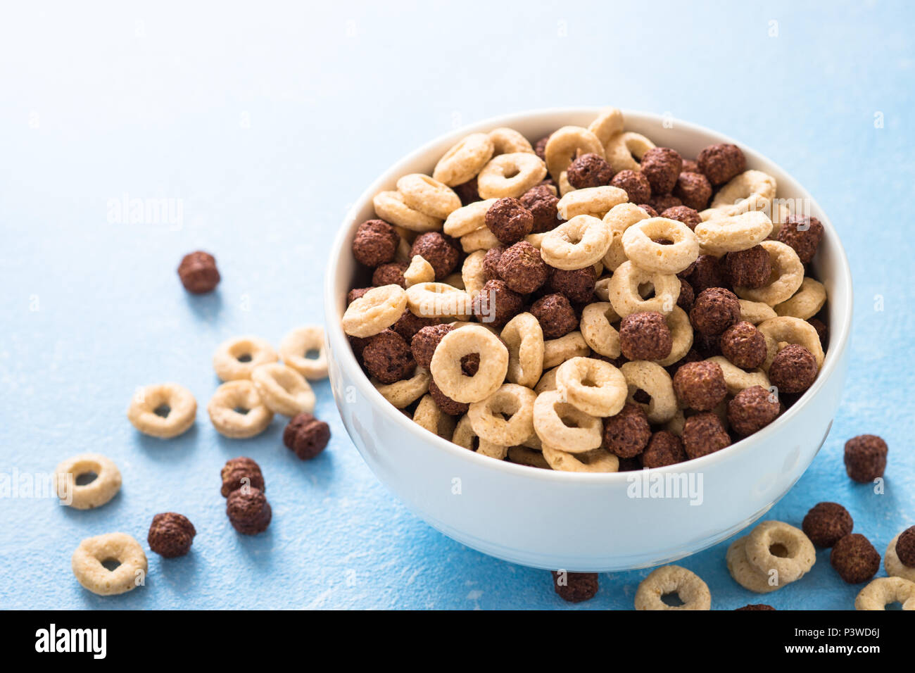 Una sana colazione di cereali sul blu. Le sfere di cioccolato e anelli di mais in bianco ciotola. Foto Stock