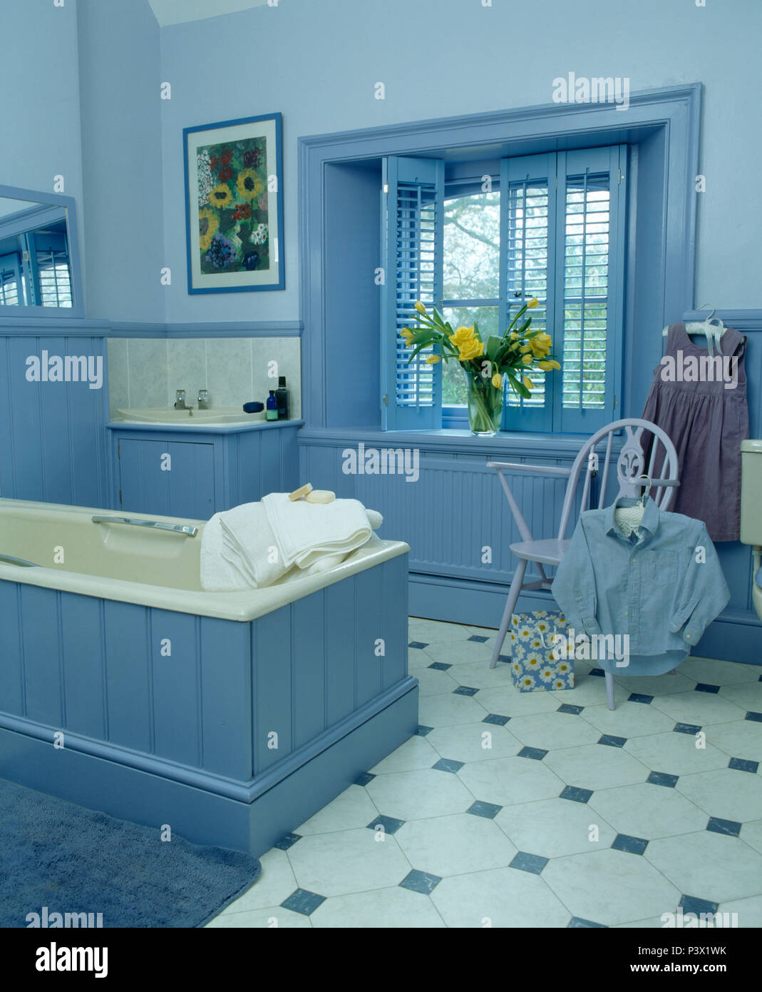 Blue persiane in stile piantagione sulla finestra in bagno di colore blu con tonque+scanalatura bagno pannellate e chequerboard pavimento piastrellato Foto Stock