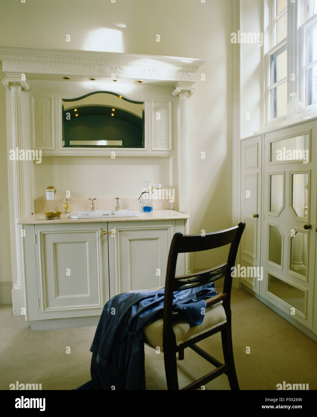 Specchio montato sopra l'unità vanity in townhouse bagno con accappatoio blu sulla sedia antica Foto Stock