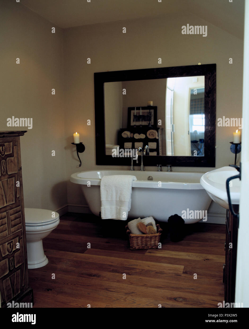 Grande specchio sopra rolltop bianco vasca nella stanza da bagno con pavimento in legno Foto Stock