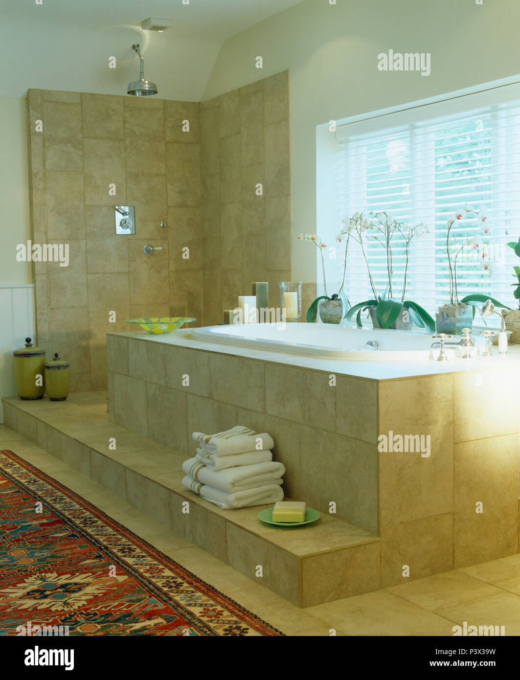 Pila di asciugamani bianchi sul passaggio al di sotto di travertino bagno piastrellato in bagno moderno con wet room doccia di stile Foto Stock