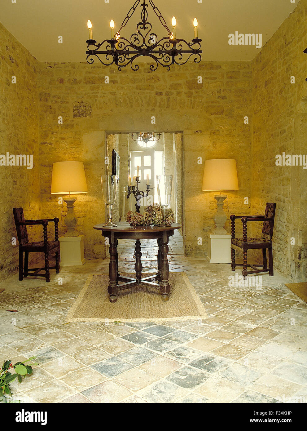 Lampade illuminate su entrambi i lati della porta nel paese francese sala da pranzo con tavolo in legno di quercia e sedie e pareti di pietra Foto Stock