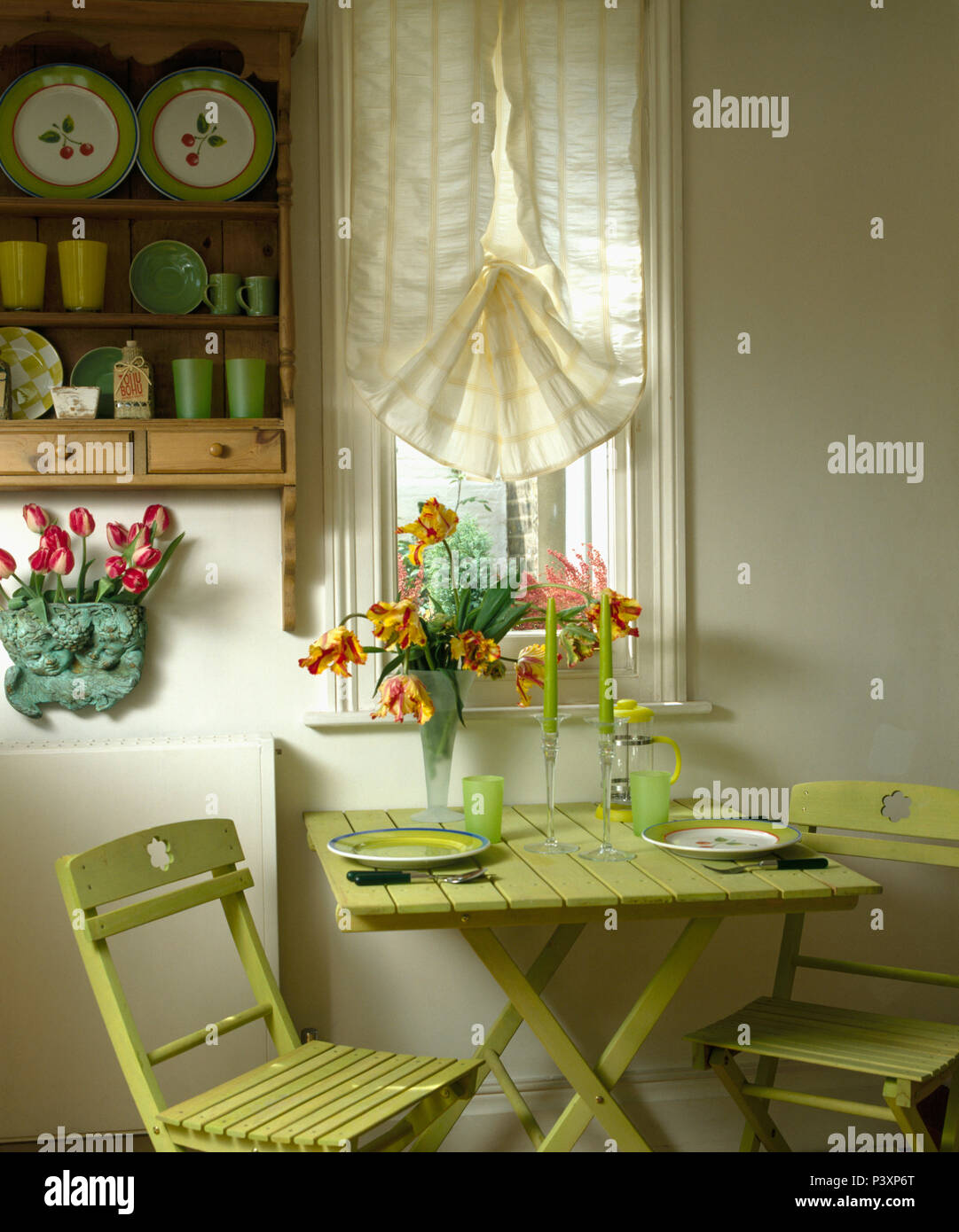 Piccolo dipinto di verde pieghevole tavolo in legno e chairsbelow piccola finestra con crema cieco in economy-sala da pranzo in stile Foto Stock