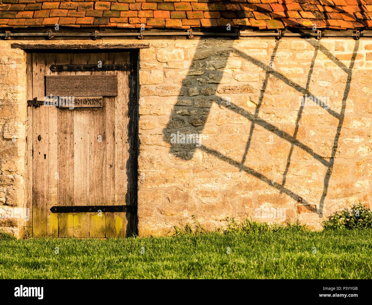 Tramonto immagine dello sportello nella parte costruita in mattoni torre del Mulino a Vento Stevington con l'ombra della vela sulla parete, Bedfordshire, Inghilterra Foto Stock