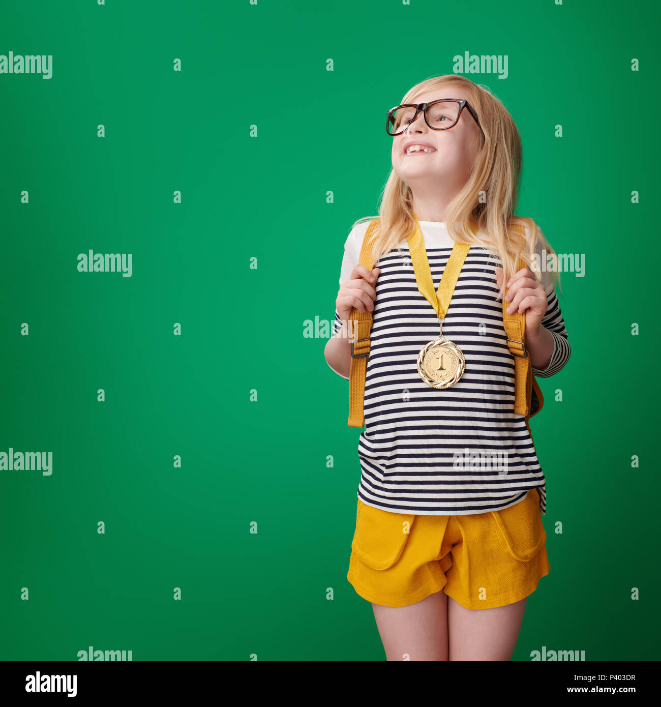 Scuola orgogliosa ragazza con zaino con medaglia d oro isolato su verde Foto Stock