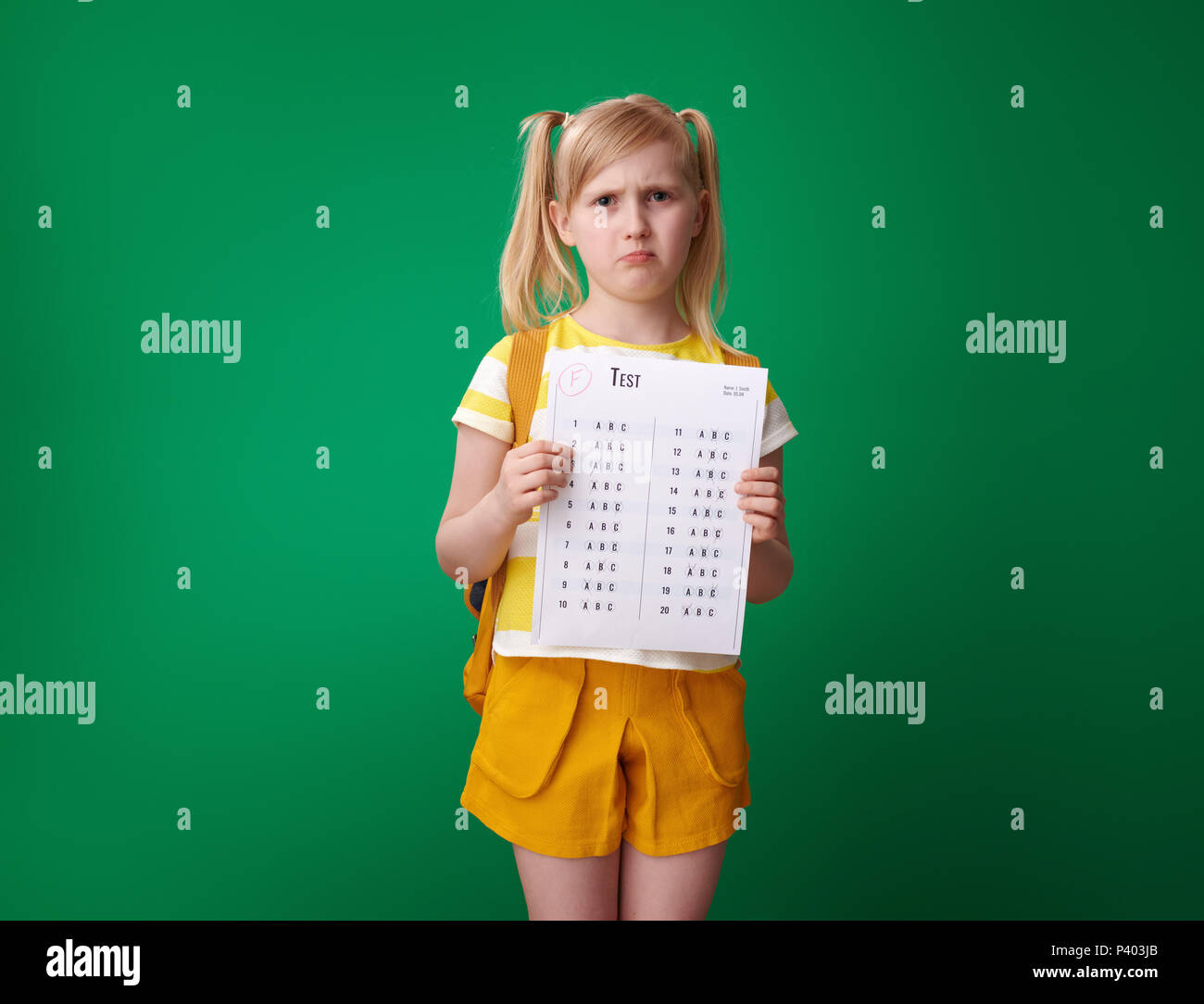 Pupilla infelice con zaino in possesso di una cattiva prova di grado isolato su sfondo verde Foto Stock