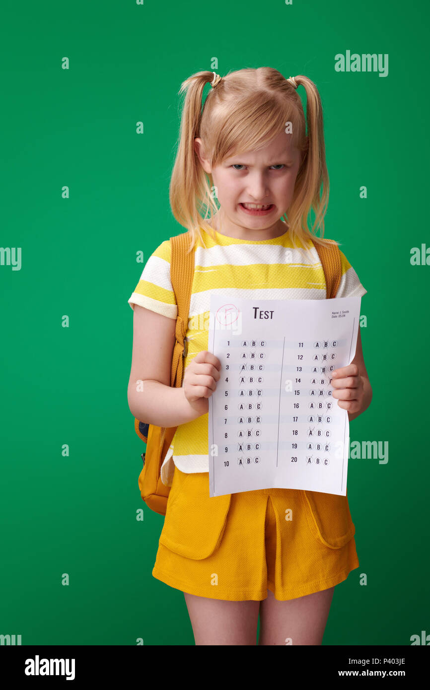 Pupilla arrabbiato con zaino ha ricevuto un pessimo grado contro lo sfondo di colore verde Foto Stock