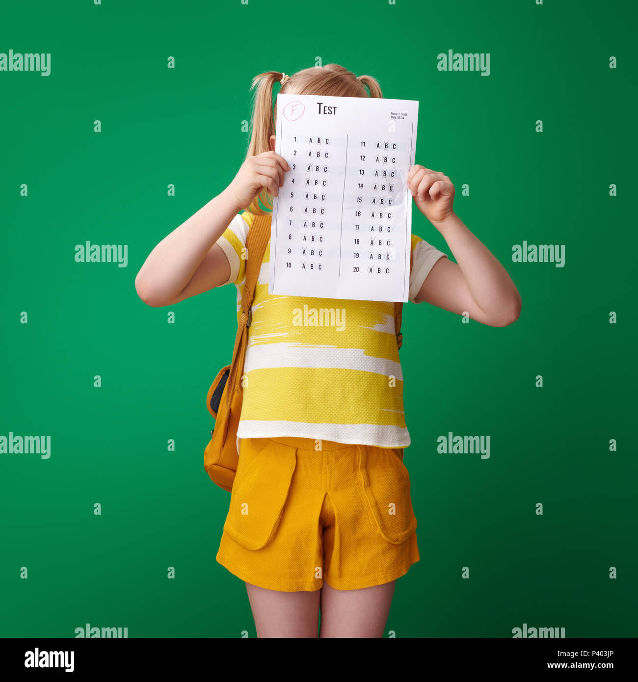 Allievo con zaino si nasconde dietro una cattiva prova di grado su sfondo verde Foto Stock