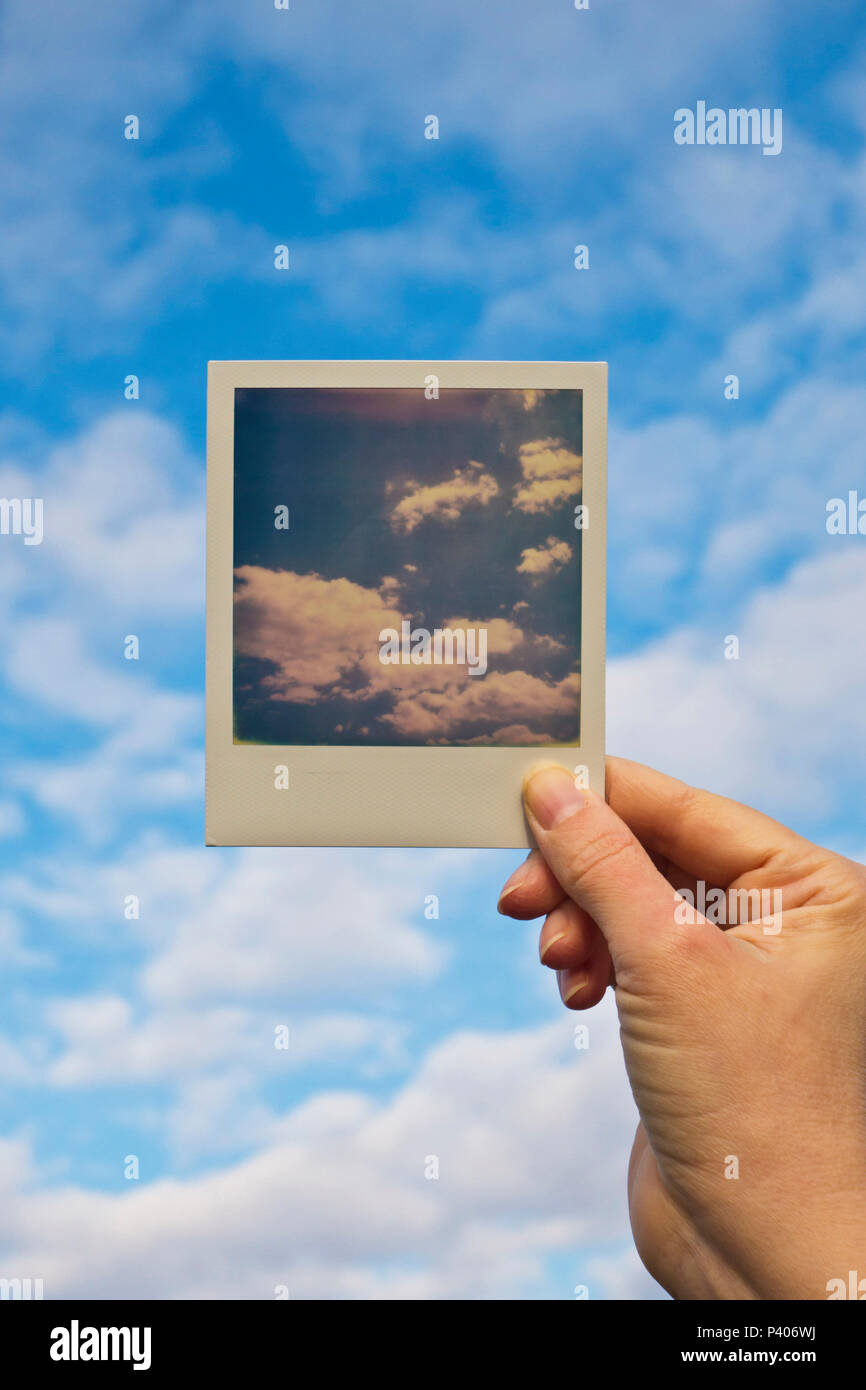 Mano che tiene una Polaroid foto di un cielo davanti del cielo Foto Stock