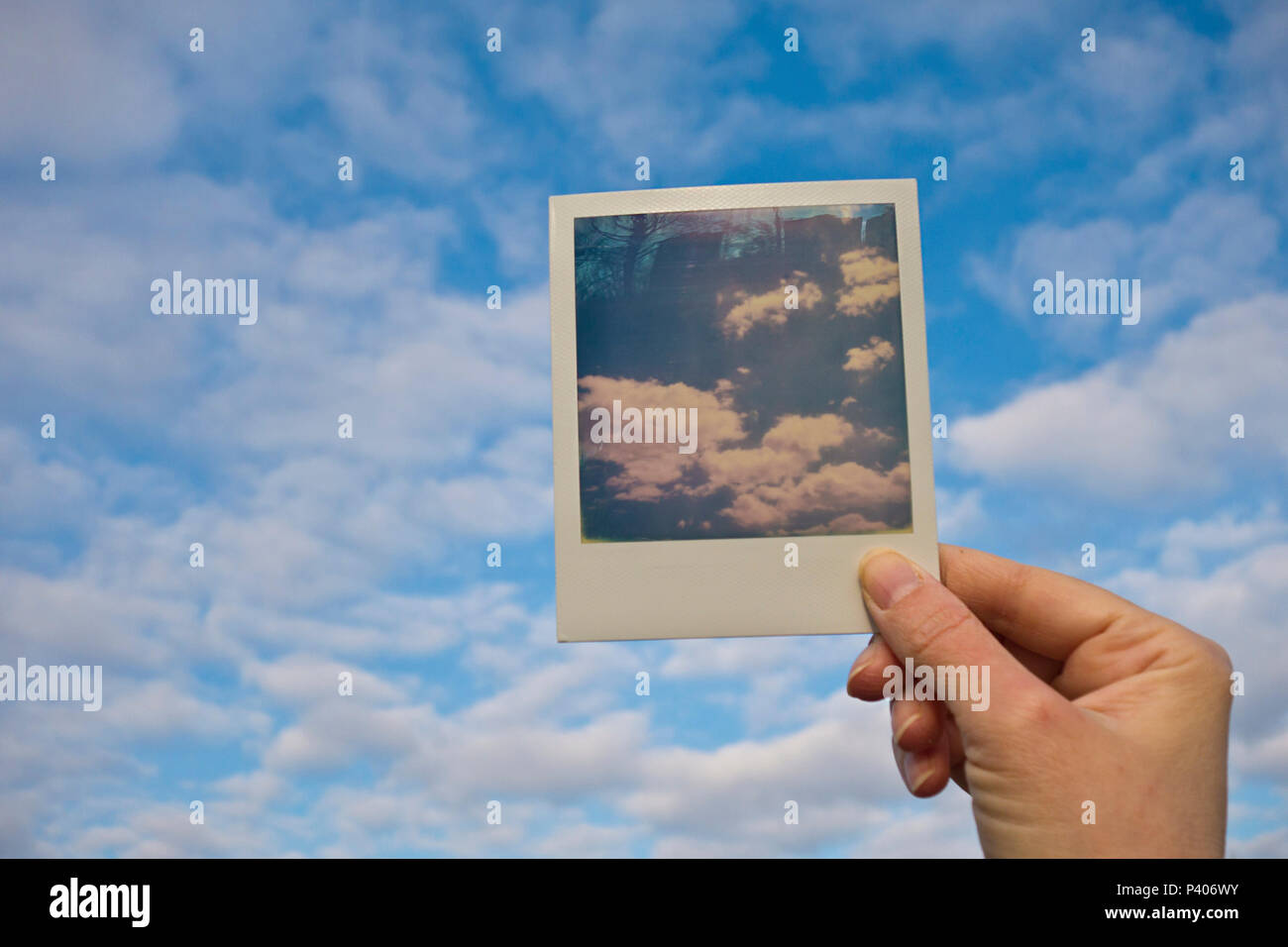 Mano che tiene una Polaroid foto di un cielo davanti del cielo Foto Stock