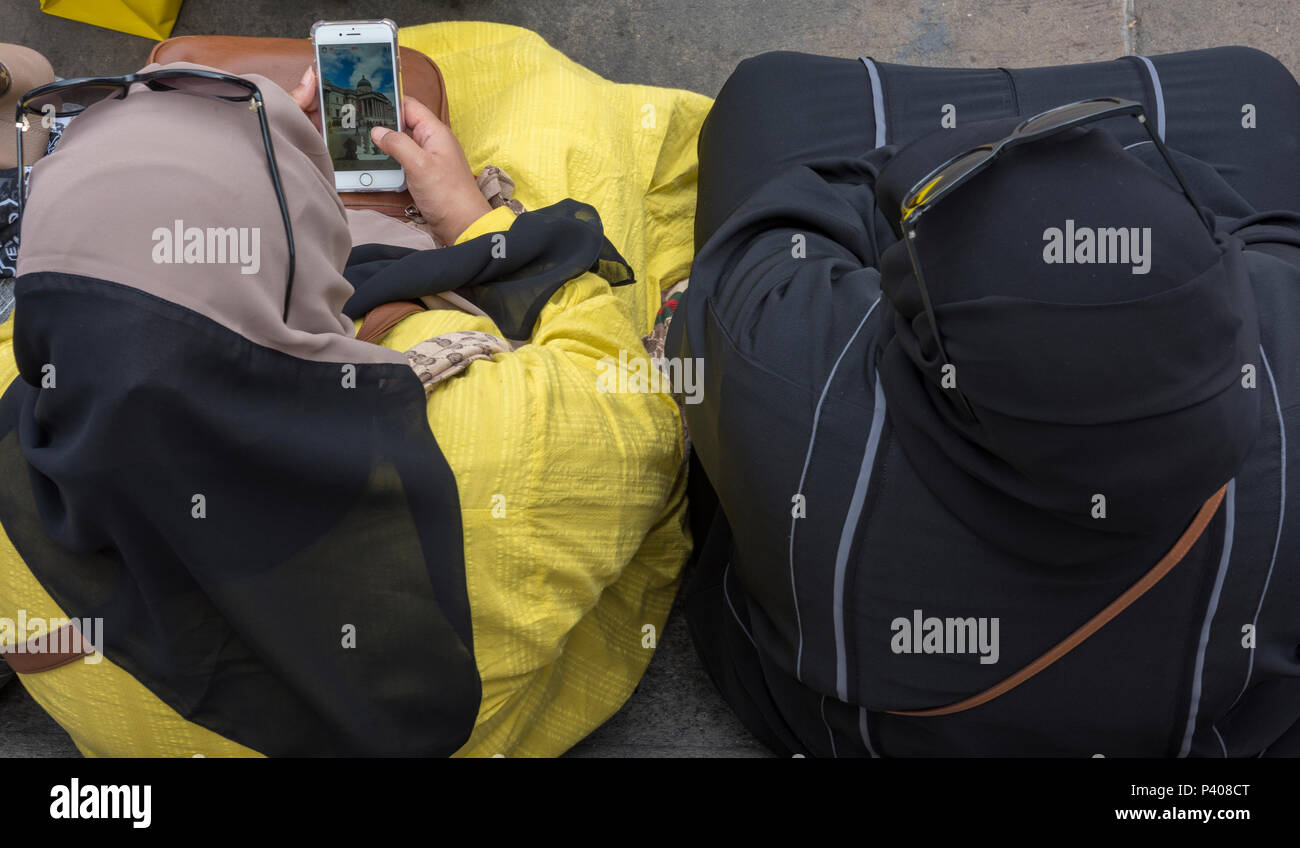 Trainare le donne musulmane seduta su una panchina in Trafalgar Square con occhiali da sole sulla parte superiore della loro il velo o abiti di testa utilizzando il telefono cellulare. la tradizione. Foto Stock