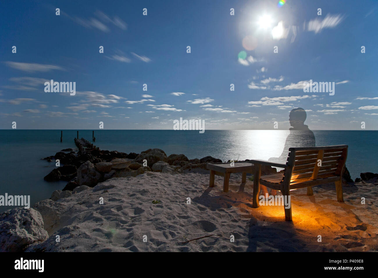 Ghost-Like uomo seduto sulla spiaggia al tramonto Foto Stock
